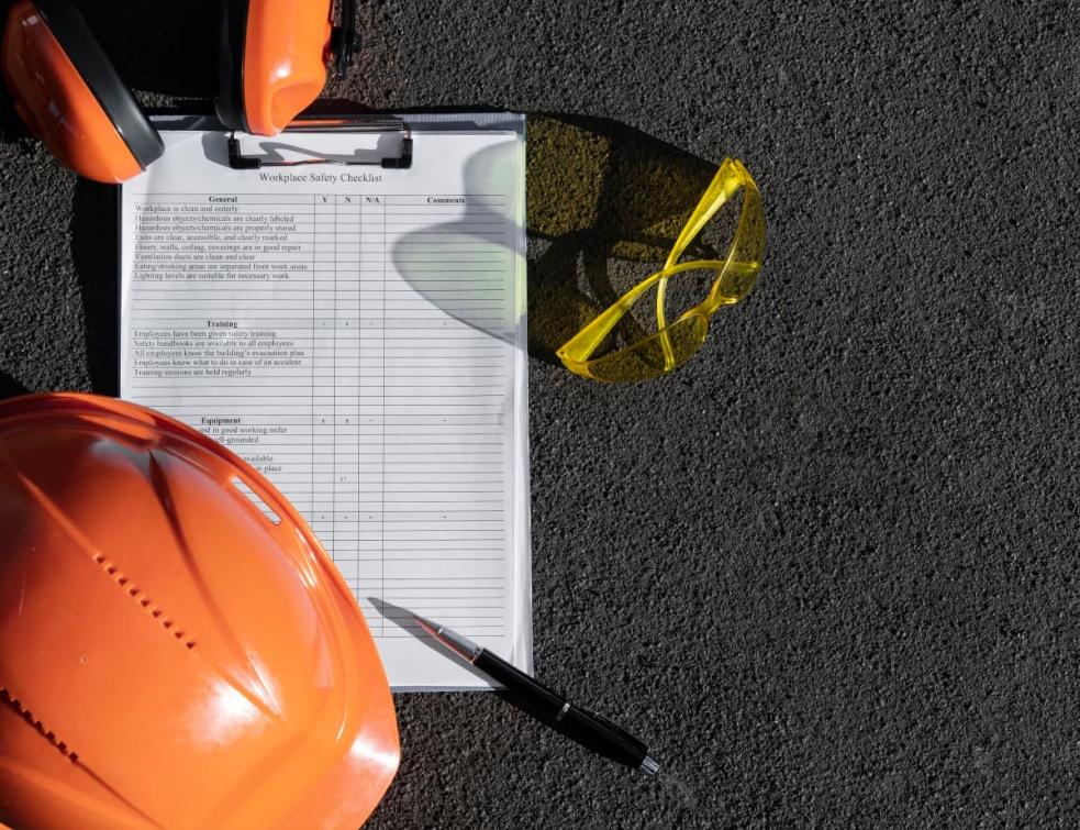 Liste de mesures de sécurité, casque et lunettes de chantier sur le sol.