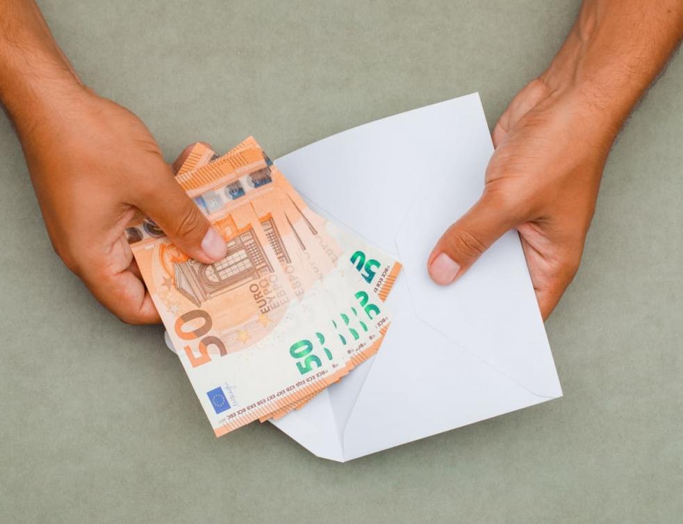Gros plan sur des billets de 50€ placés dans une enveloppe par un homme