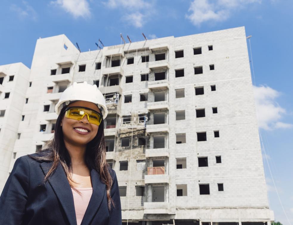 femme avec casque de chantier souriant devant un bâtiment en cours de construction