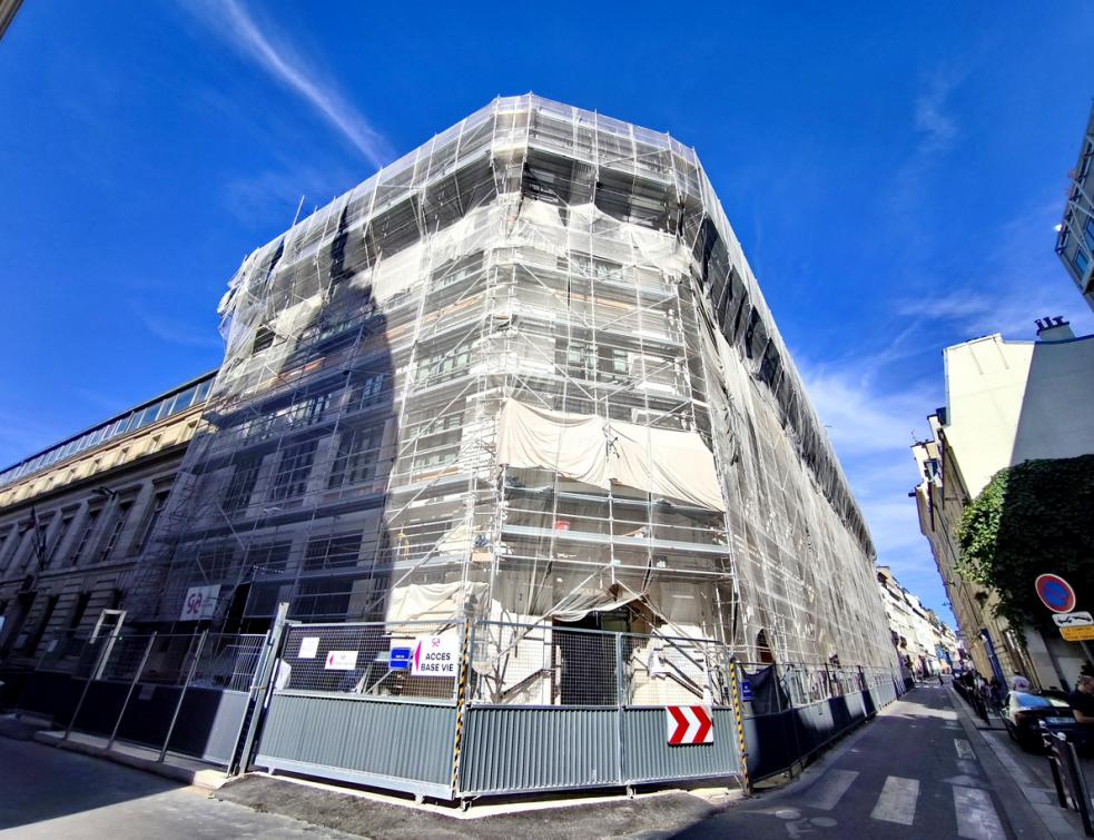le bâtiment en cours de restructuration, ceinturé d'échafaudages et protégé par des bâches étanches